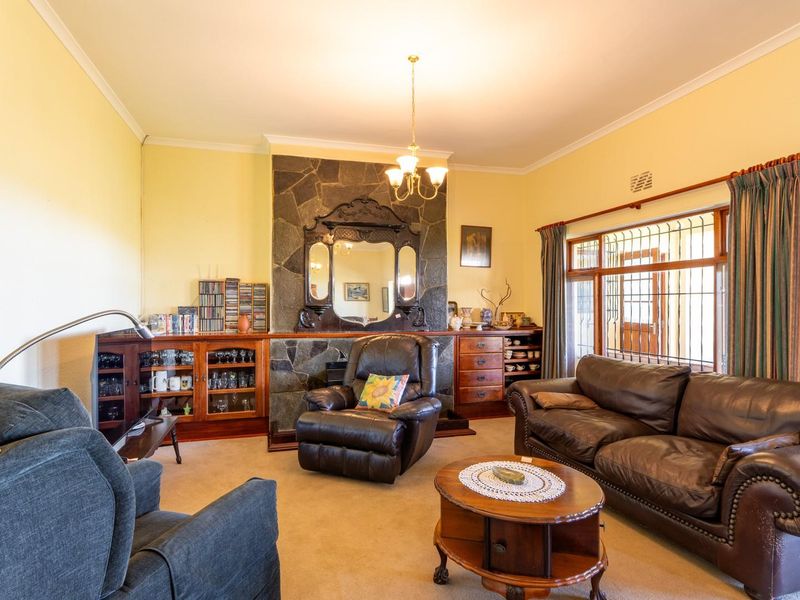 A traditional living room featuring a prominent stone fireplace, built-in wooden cabinetry, and large windows with security bars.
