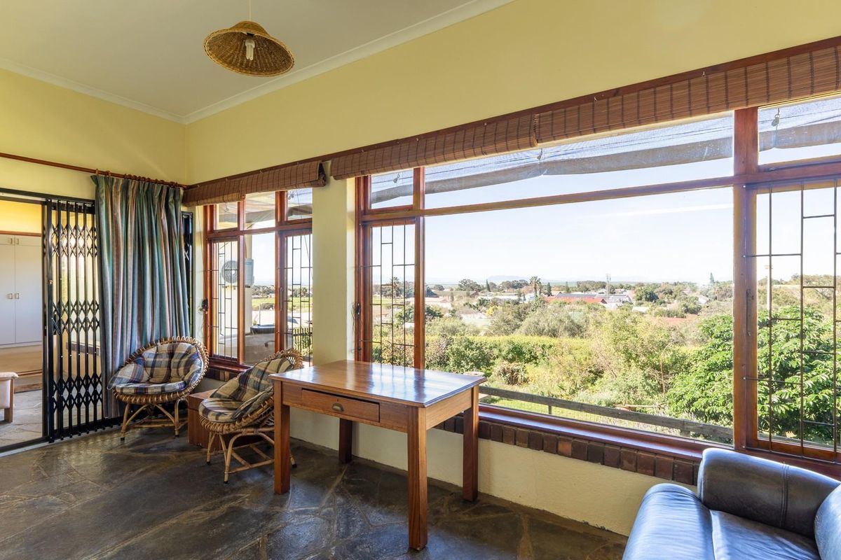 A sunlit living area featuring large picture windows with scenic views, stone flooring, and direct access to adjacent rooms through a security gate.