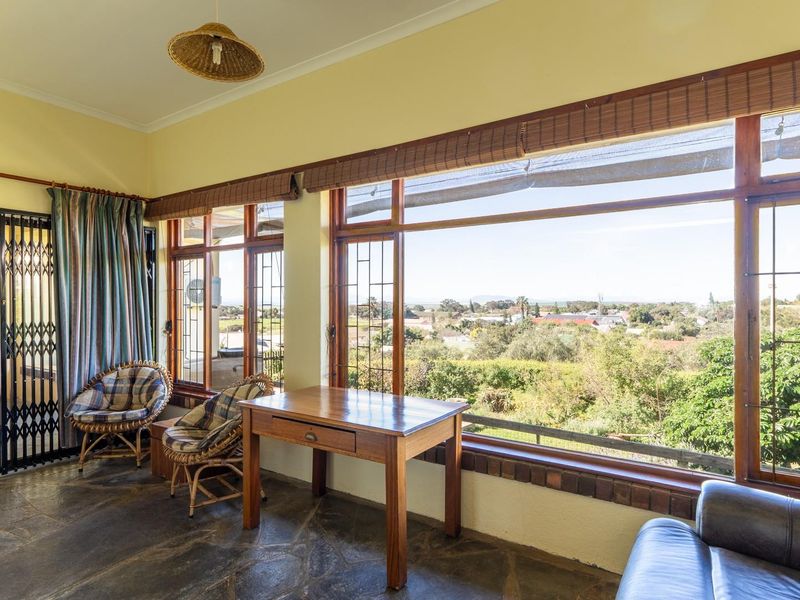 A sunlit living area featuring large picture windows with scenic views, stone flooring, and direct access to adjacent rooms through a security gate.
