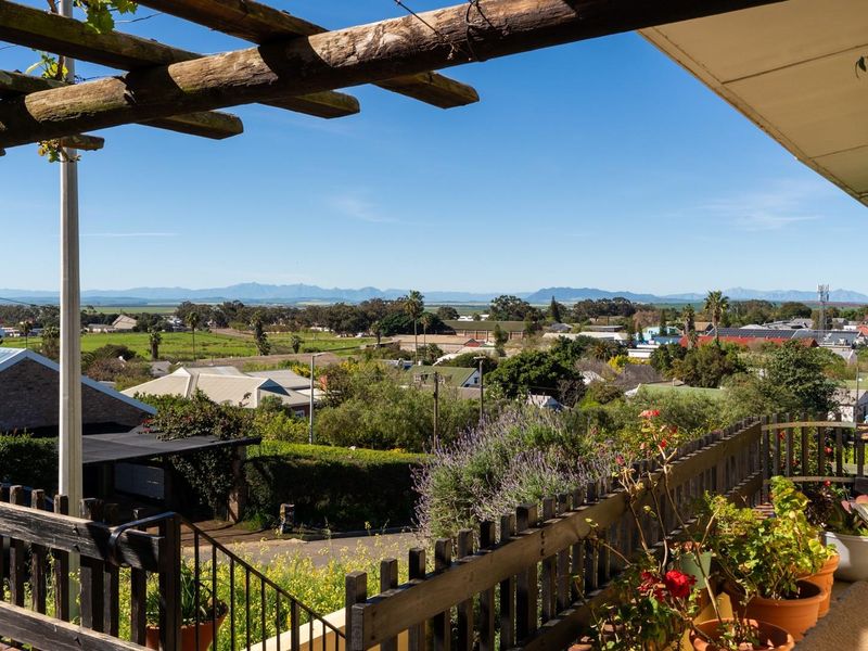 An elevated patio featuring a timber pergola and balustrade, offering expansive panoramic views over the surrounding neighborhood and distant mountain range.