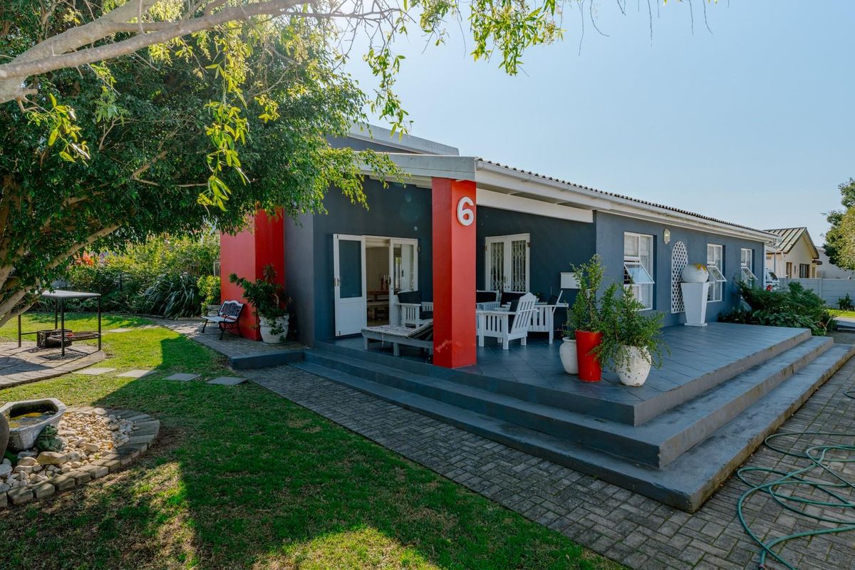 A well-maintained rear exterior view featuring a spacious covered patio, paved walkway, and established garden area.