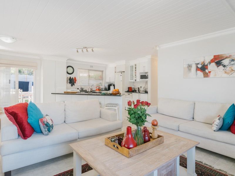 Bright open-plan living and kitchen area featuring white cabinetry, stone countertops, and a modern tongue and groove ceiling with direct access to the patio.