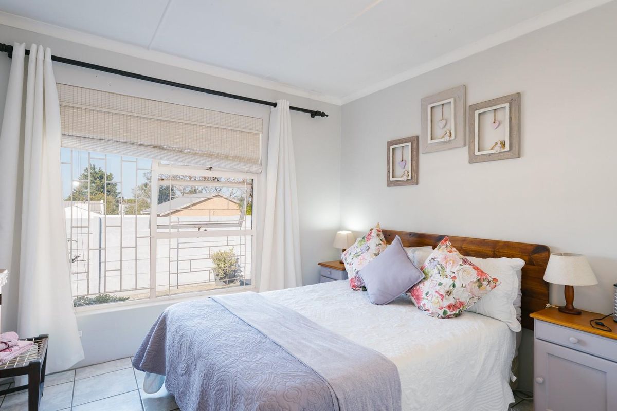 A well-maintained bedroom featuring tiled flooring and a window fitted with security bars, offering a bright and comfortable living space.