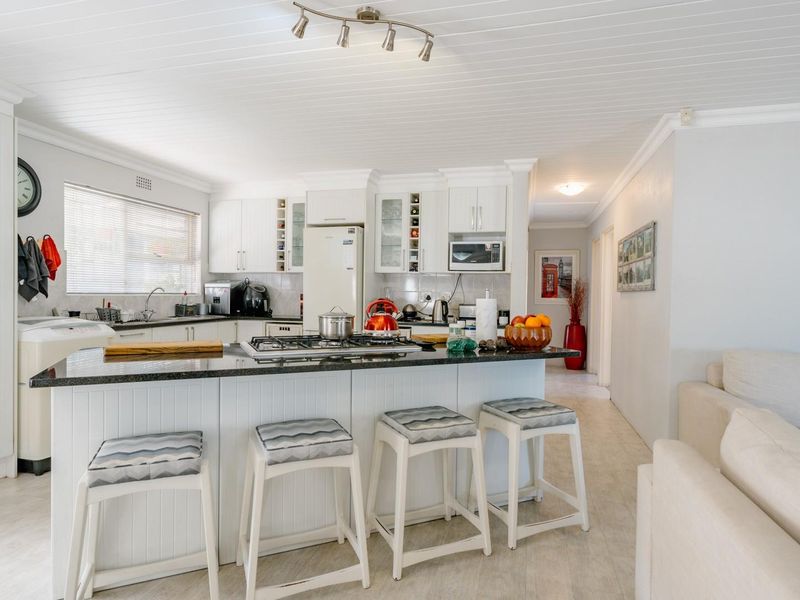 Bright open-plan kitchen featuring a central island with a gas cooktop, granite countertops, and ample white cabinetry, seamlessly flowing into the living area.