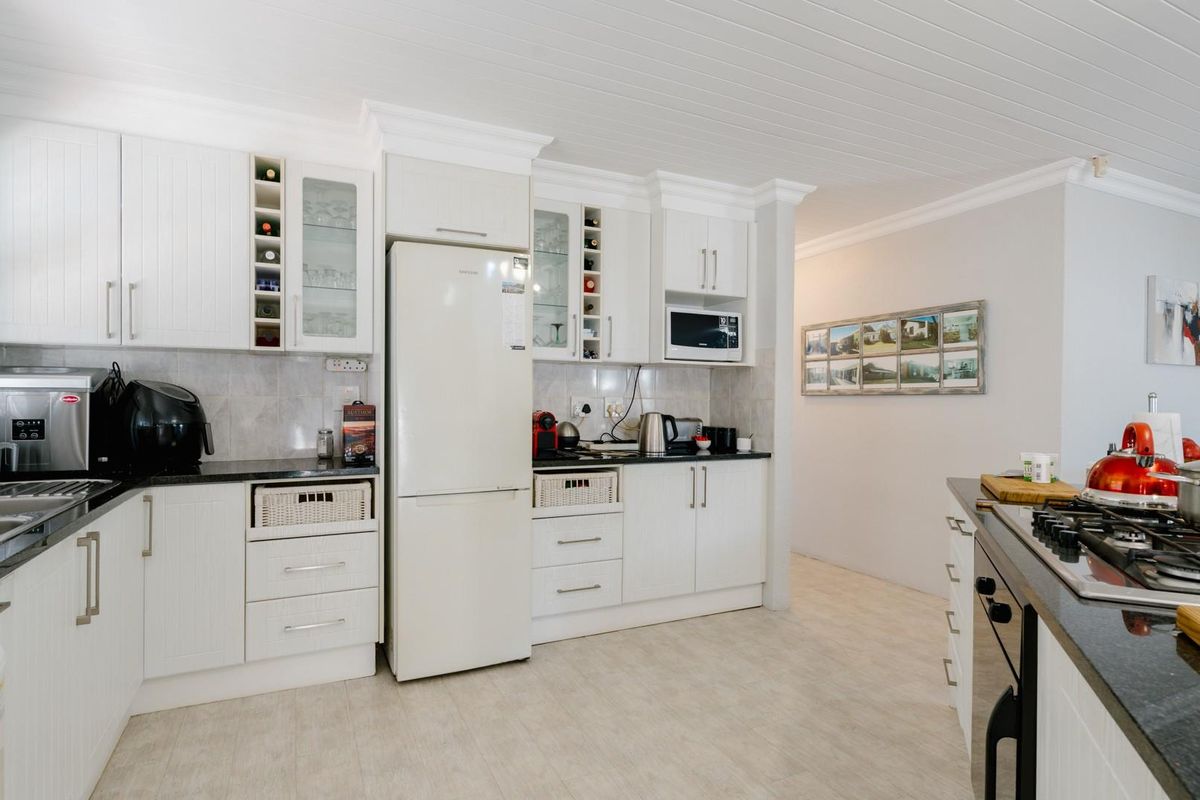 A well-maintained kitchen featuring white cabinetry, black granite countertops, a gas hob, built-in oven, and a classic tongue and groove ceiling.