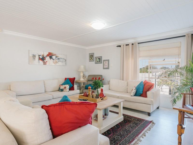 A bright and comfortable living room featuring a tongue and groove ceiling, cove cornicing, and a large louvered window allowing natural light.