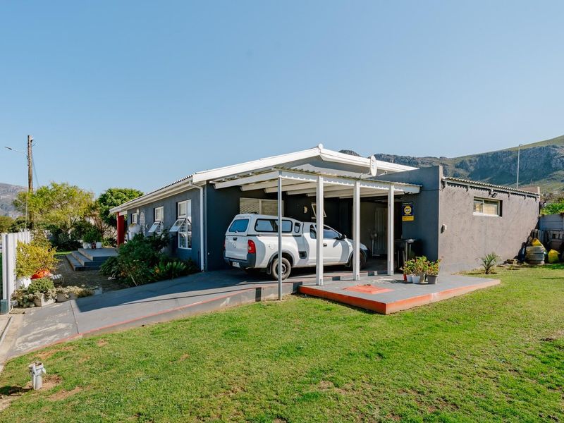 Front exterior view of the house featuring a covered carport, concrete driveway, and established garden area with mountain views.