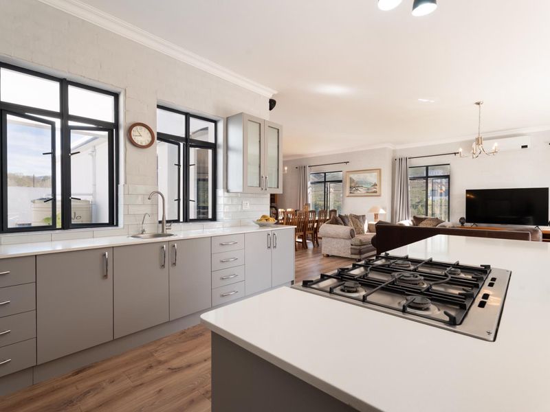 Modern open-plan kitchen and living area featuring a central island with gas cooktop, sleek cabinetry, and light-toned laminate flooring.