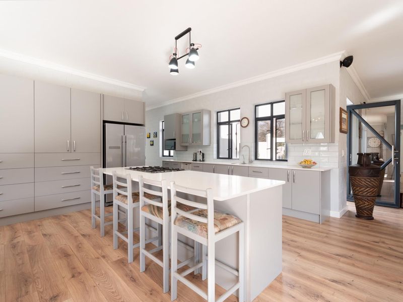 Modern, well-appointed kitchen featuring a central island with gas hob, stone countertops, ample cabinetry, and stylish laminate flooring in a bright, open layout.