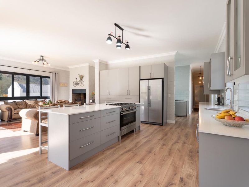 Modern open-plan kitchen and living area featuring a central island, gas stove, sleek cabinetry, and warm laminate flooring, flowing into a comfortable lounge space.
