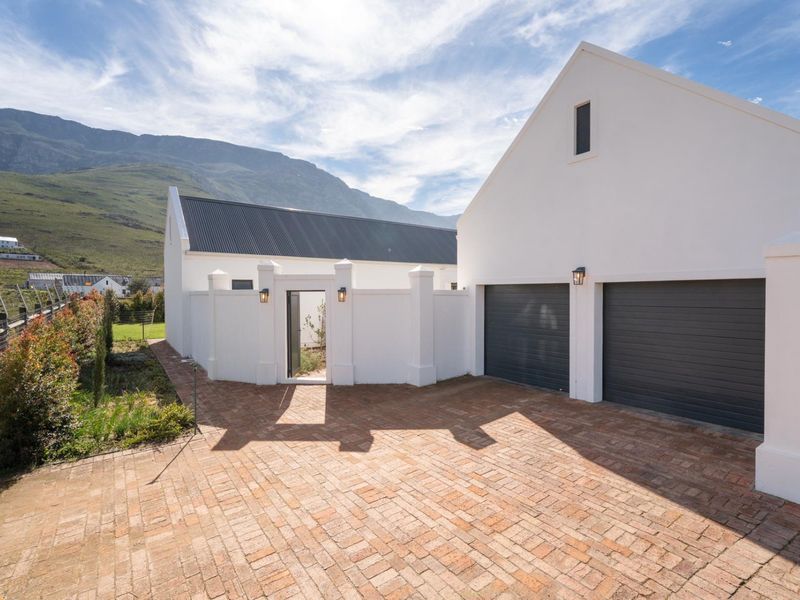 A well-maintained modern home exterior featuring a double garage, brick-paved driveway, and a secure pedestrian entrance, set against a scenic mountain backdrop.