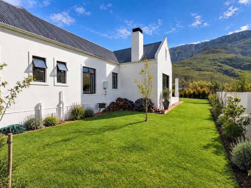 A well-maintained rear garden featuring a manicured lawn, white exterior facade, and mountain views.