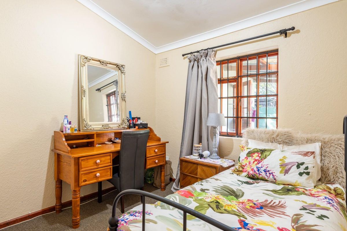 A cozy bedroom featuring carpeted flooring, coving, and a window fitted with security bars, providing a functional and comfortable living space.