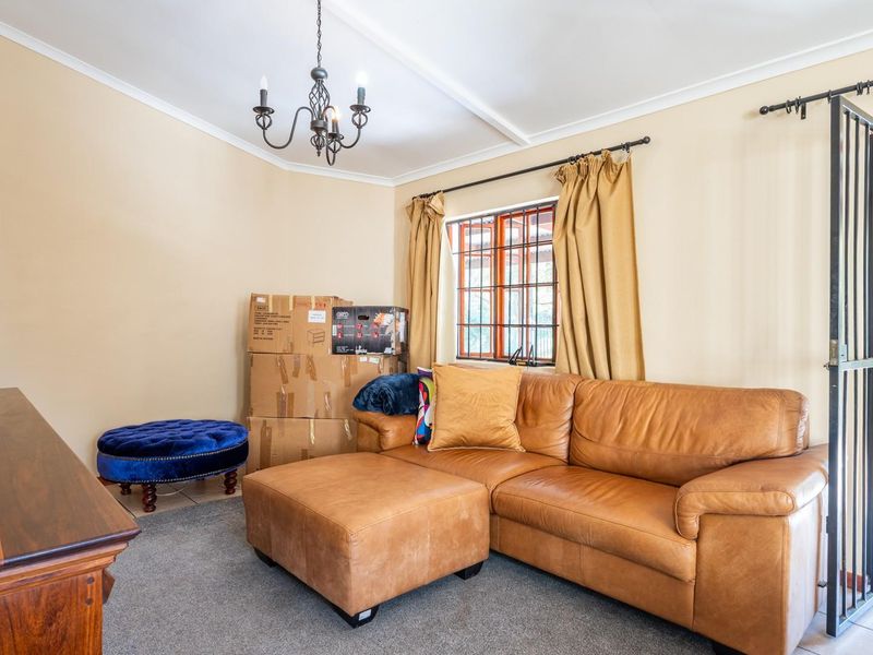 A living room featuring tiled and carpeted flooring, a chandelier, and direct access to an outdoor patio area through a security gate.