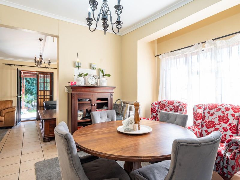 A bright dining room featuring tiled flooring, a classic wrought iron chandelier, and a sliding glass door leading to an adjacent living area.