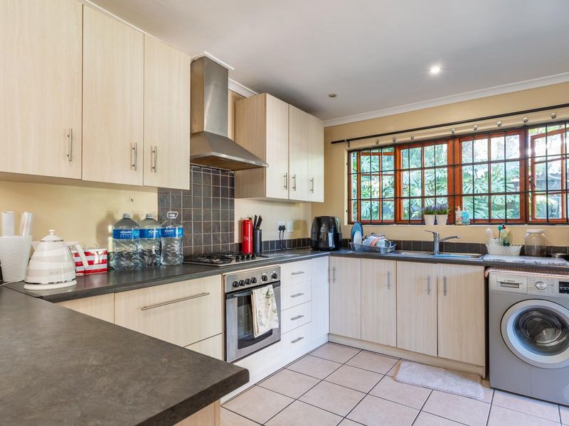 A functional kitchen featuring light wood-finish cabinetry, dark countertops, a built-in oven with gas hob, and integrated laundry plumbing.
