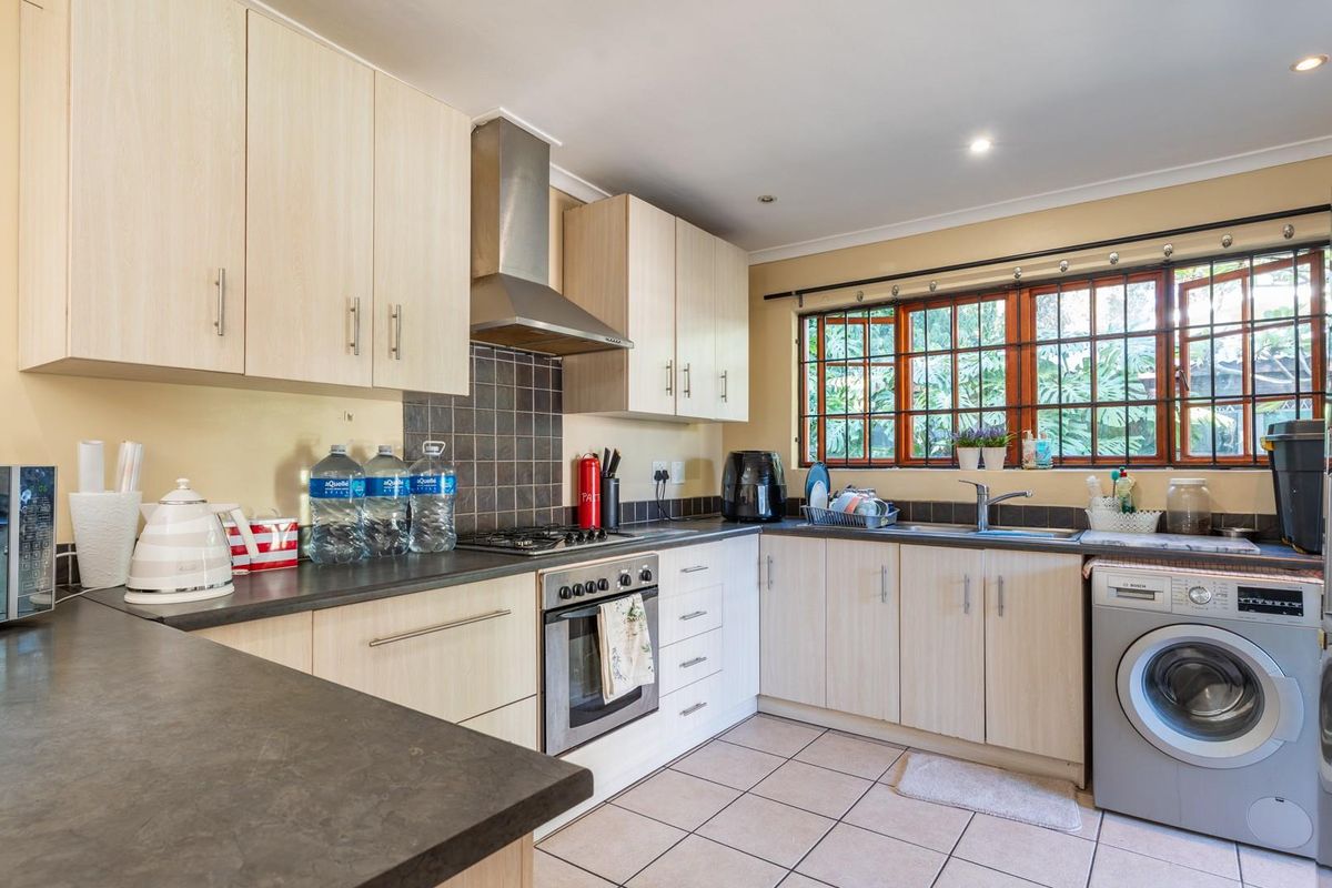 A functional kitchen featuring light wood-finish cabinetry, dark countertops, a built-in oven with gas hob, and integrated laundry plumbing.
