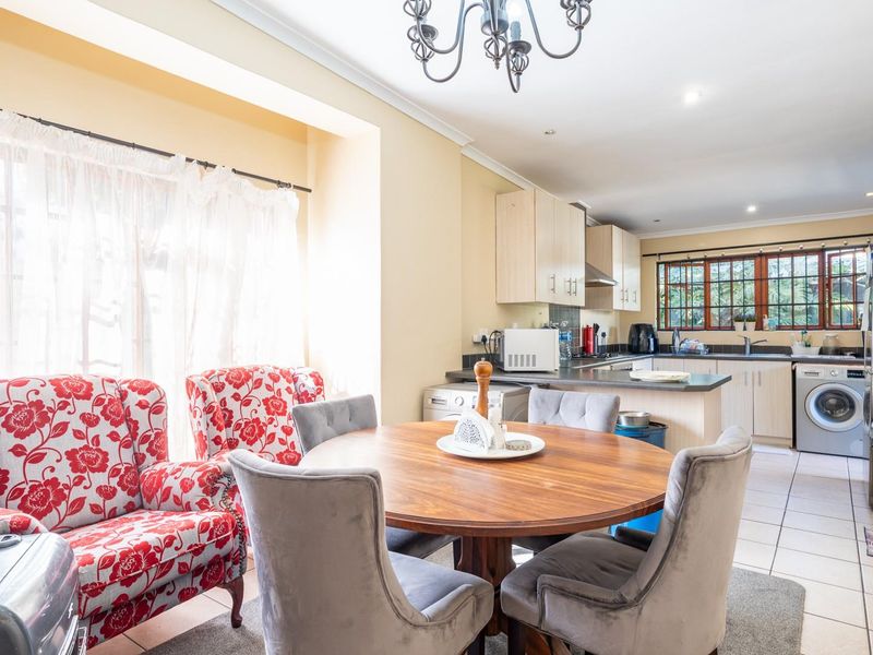 Open-plan kitchen and dining area featuring light-toned cabinetry, tiled flooring, and natural light from large windows.