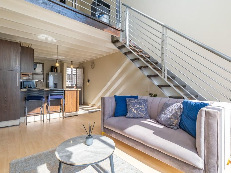 Open-plan living area featuring a modern staircase with metal balustrades, laminate flooring, and a compact kitchen with dark wood cabinetry.