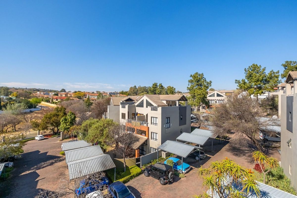 An aerial view of the apartment complex featuring covered parking bays, paved driveways, and multi-story residential units with tiled roofs.