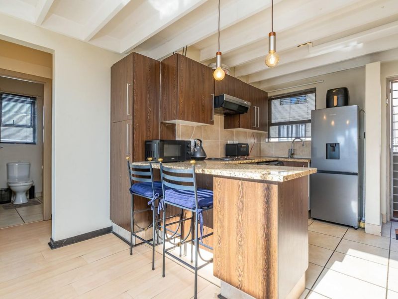 Compact kitchen featuring dark wood cabinetry, granite countertops, exposed ceiling beams, and an adjacent bathroom entrance.
