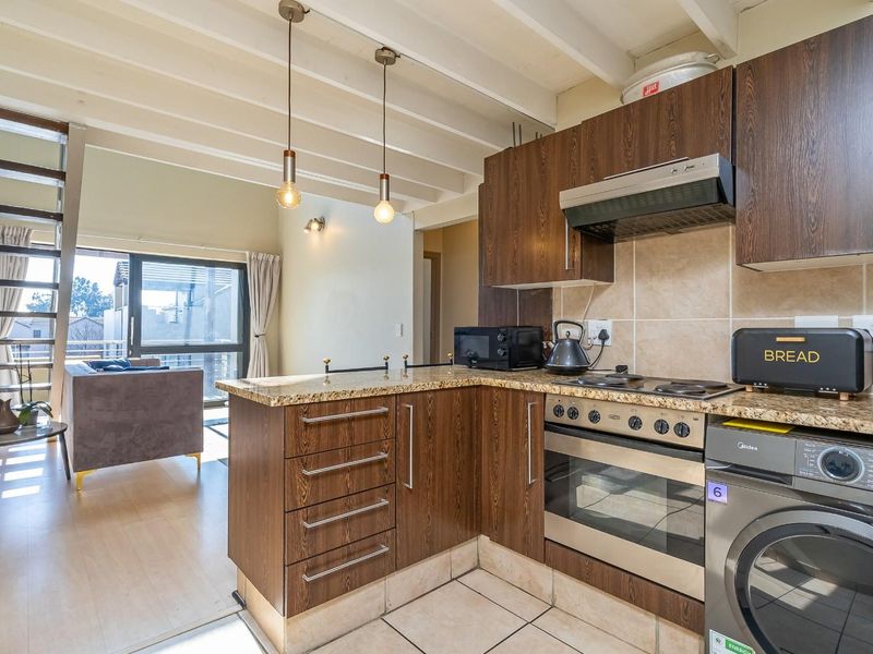 Open plan kitchen featuring dark wood cabinetry, granite countertops, and integrated appliances, flowing into a living area with a staircase and access to a balcony.
