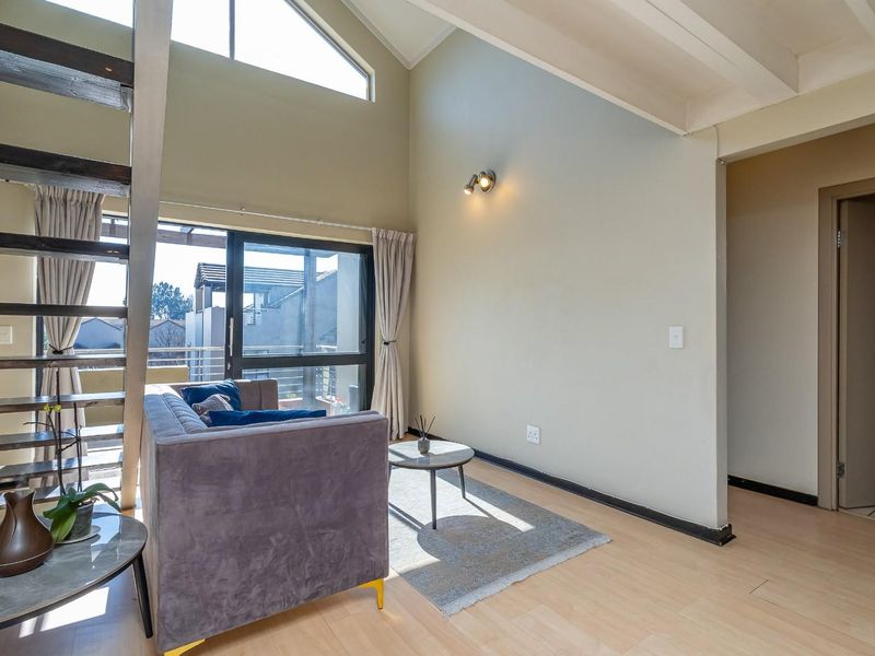 Bright living room featuring a vaulted ceiling with exposed beams, laminate flooring, and a staircase leading to an upper level.