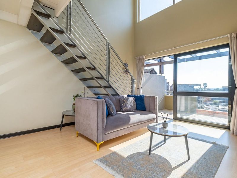 Bright double-volume living area featuring a modern staircase with metal balustrade and large sliding glass doors leading to an outdoor balcony.