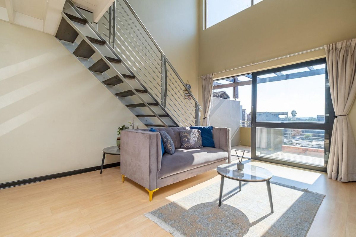 Bright double-volume living area featuring a modern staircase with metal balustrade and large sliding glass doors leading to an outdoor balcony.