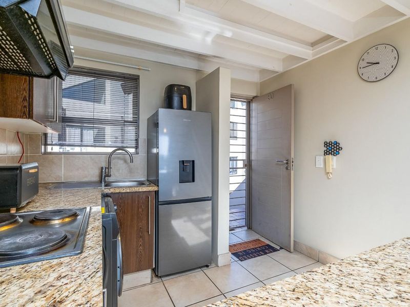 Compact kitchen featuring granite countertops, electric hob, extractor fan, and tiled flooring, with direct access to an exterior entrance.