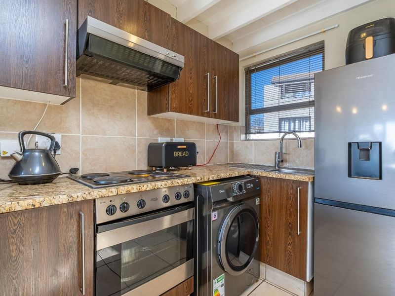 A functional kitchen featuring wood-look cabinetry, granite countertops, a built-in oven with hob, and an integrated laundry appliance space.