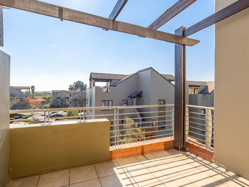 A spacious balcony featuring a timber pergola, tiled flooring, and metal balustrades, offering an open outdoor area with views of the surrounding complex.
