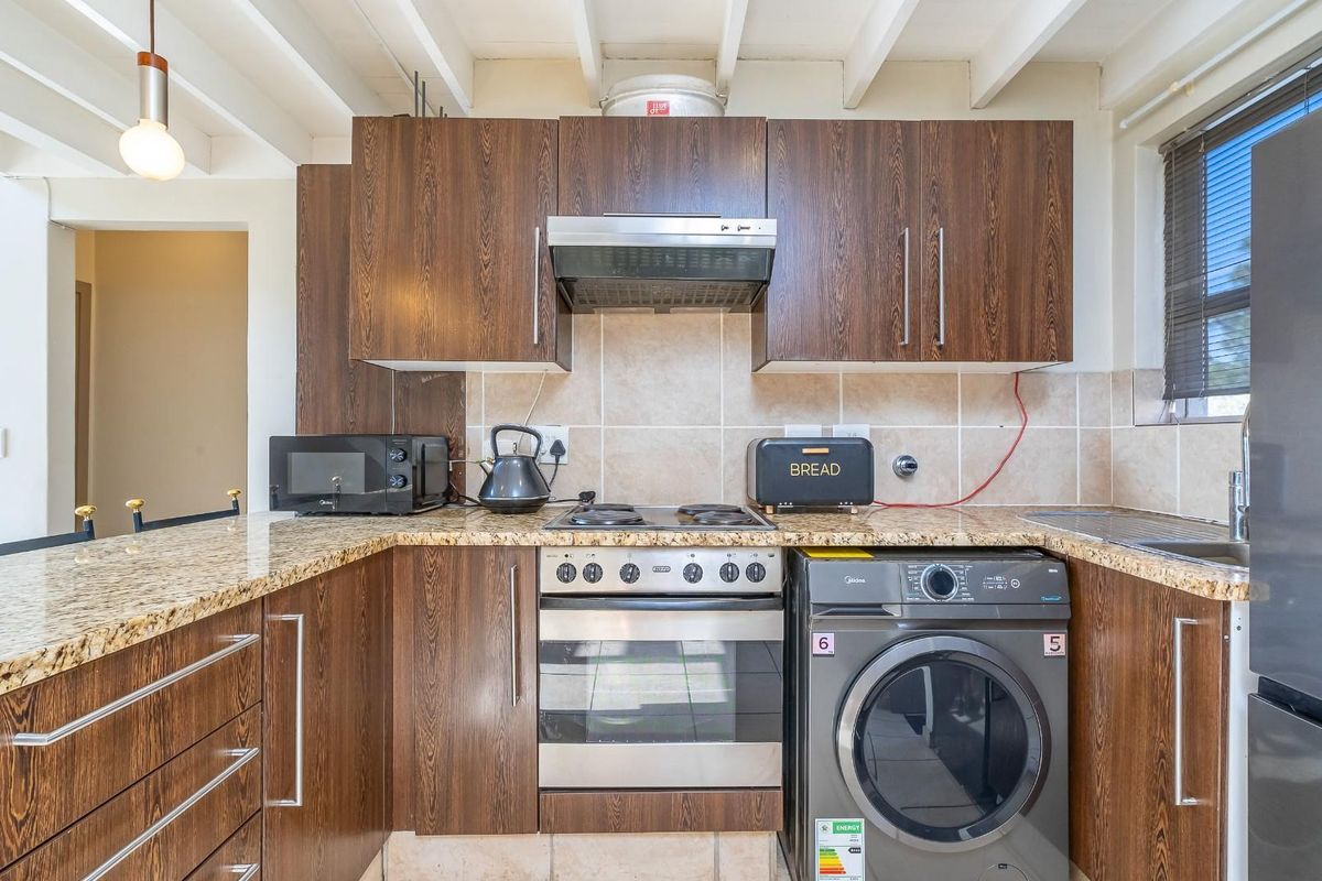 A functional kitchen featuring wood-finish cabinetry, granite countertops, a tiled backsplash, and exposed beam ceilings, providing a practical and well-lit cooking space.