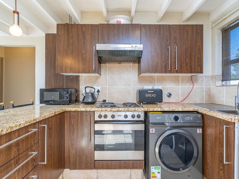 A functional kitchen featuring wood-finish cabinetry, granite countertops, a tiled backsplash, and exposed beam ceilings, providing a practical and well-lit cooking space.