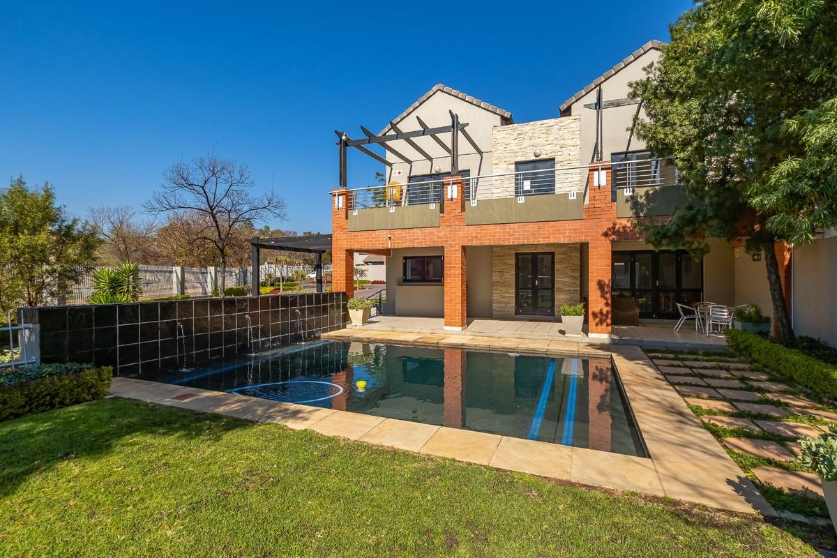 Rear exterior view of the apartment featuring a swimming pool, water feature, brick pillars, and an upper-level balcony with a pergola.