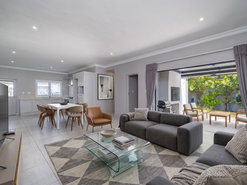 Spacious open-plan living and kitchen area featuring modern tiled floors, recessed lighting, and seamless flow to a covered outdoor patio with a built-in fireplace.