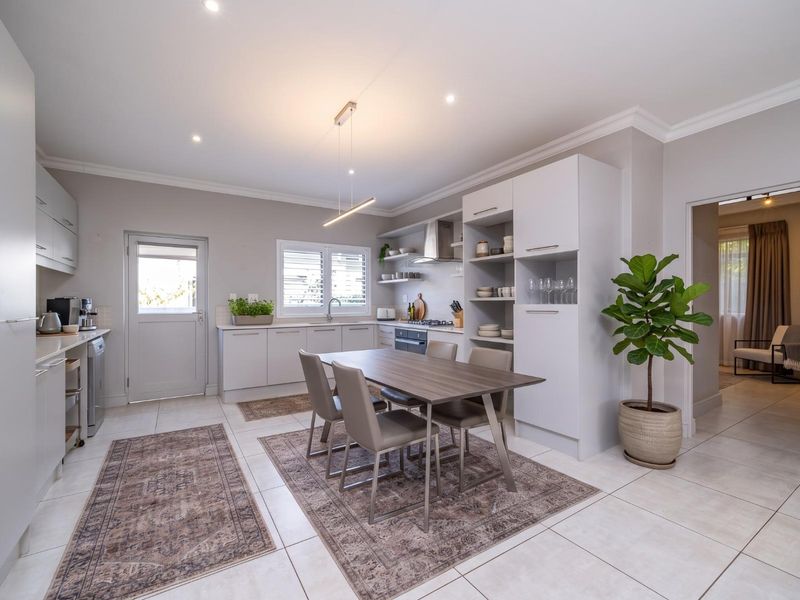 Modern open-plan kitchen and dining area featuring sleek built-in cabinetry, integrated appliances, tiled flooring, and recessed lighting, creating a bright and functional living space.