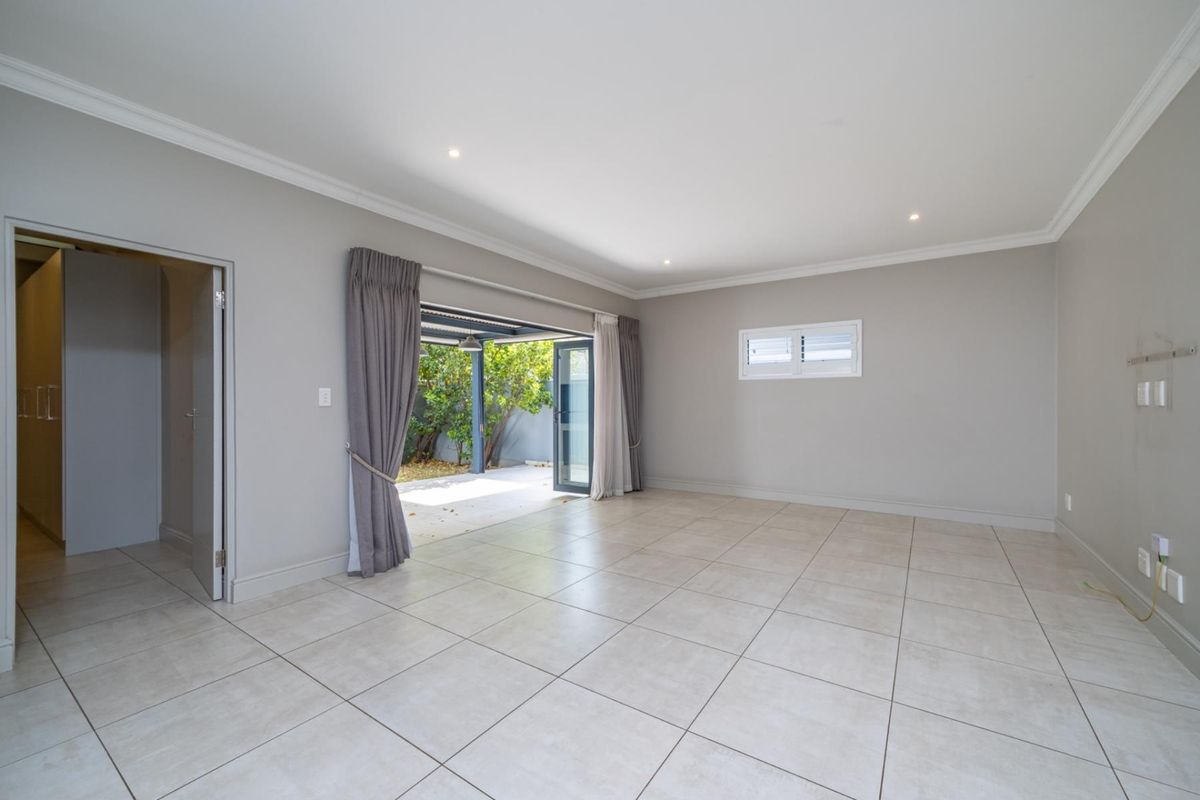 Spacious, light-filled living area featuring neutral tiled flooring, recessed lighting, and seamless access to an outdoor patio through large sliding glass doors.