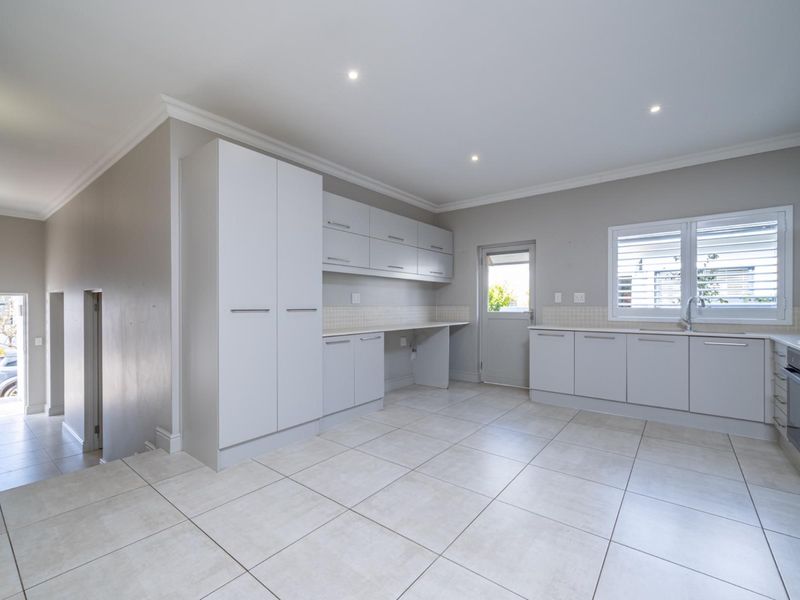 A clean, modern kitchen featuring white built-in cabinetry, tiled flooring, integrated appliances, and a tiled backsplash with direct access to the exterior.