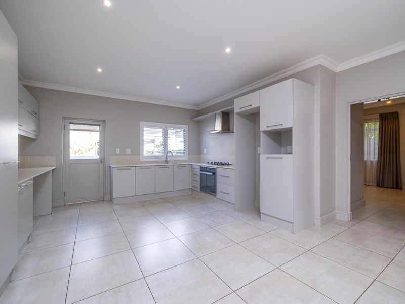 A clean, modern kitchen featuring neutral cabinetry, tiled flooring, built-in gas hob, oven, and extractor fan with direct access to the exterior.