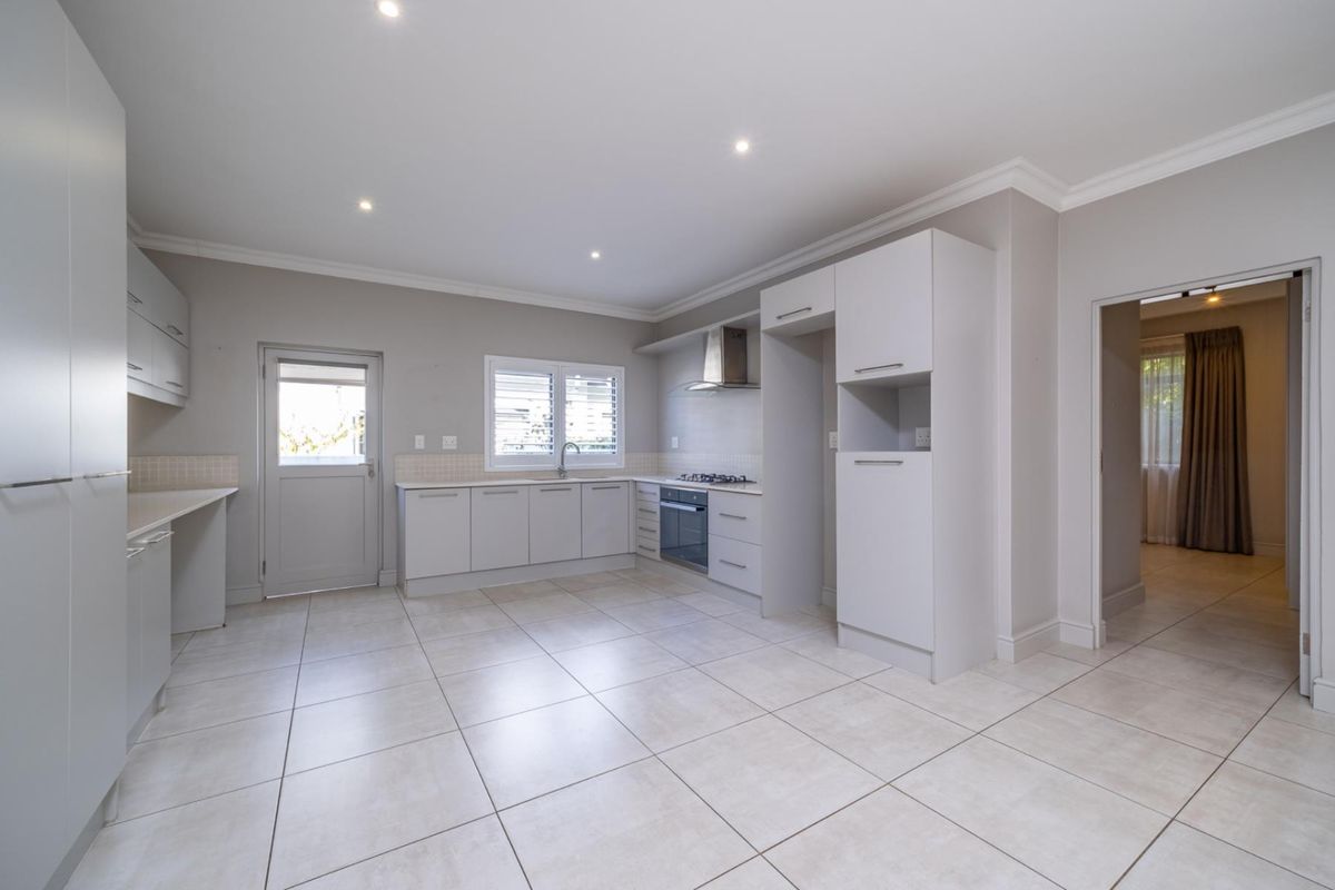 A clean, modern kitchen featuring neutral cabinetry, tiled flooring, built-in gas hob, oven, and extractor fan with direct access to the exterior.