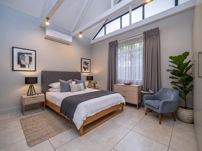 Spacious bedroom featuring high vaulted ceilings with exposed rafters, clerestory windows for natural light, tiled flooring, and a split-system air conditioner.