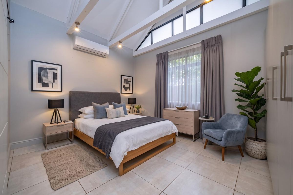Spacious bedroom featuring high vaulted ceilings with exposed rafters, clerestory windows for natural light, tiled flooring, and a split-system air conditioner.