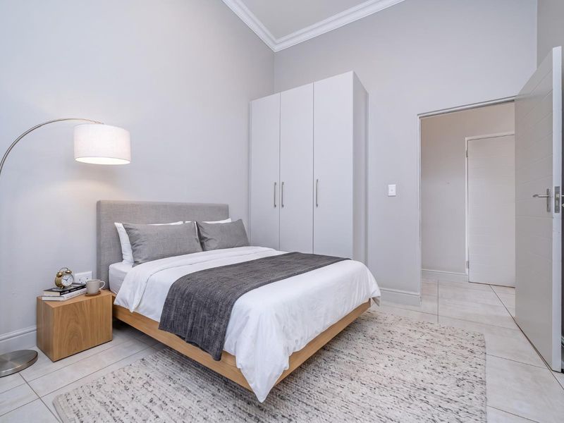 A modern, well-maintained bedroom featuring neutral tones, tiled flooring, and a built-in wardrobe with clean architectural lines.