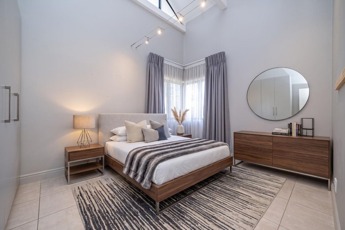 A well-maintained bedroom featuring a high vaulted ceiling, modern track lighting, tiled flooring, and a built-in wardrobe.