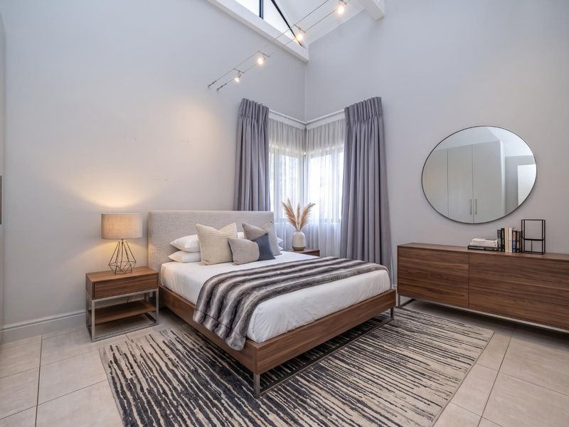 A well-maintained bedroom featuring a high vaulted ceiling, modern track lighting, tiled flooring, and a built-in wardrobe.