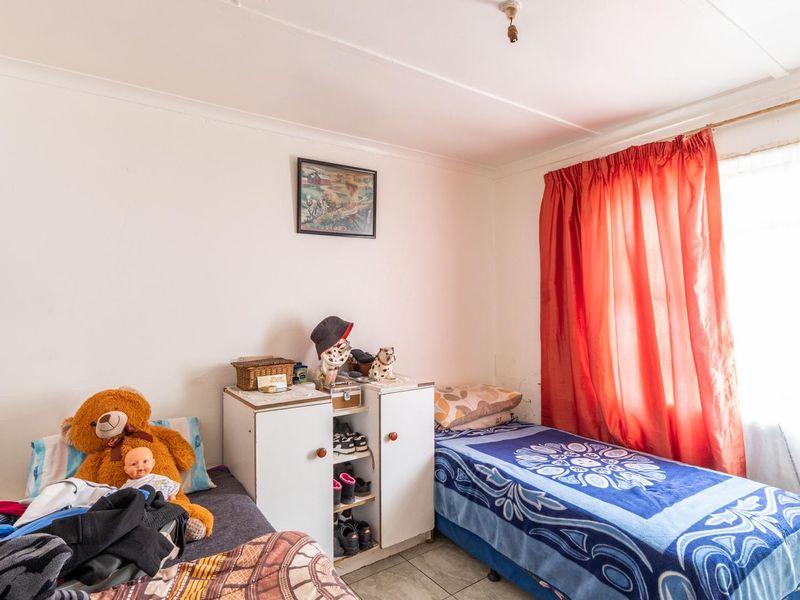 A functional bedroom featuring tiled flooring and a window with a curtain rail, offering a simple and practical living space.