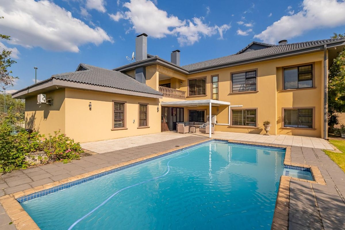 Rear view of the property featuring a swimming pool, paved patio area, balcony, and well-maintained exterior facade with a tiled roof.