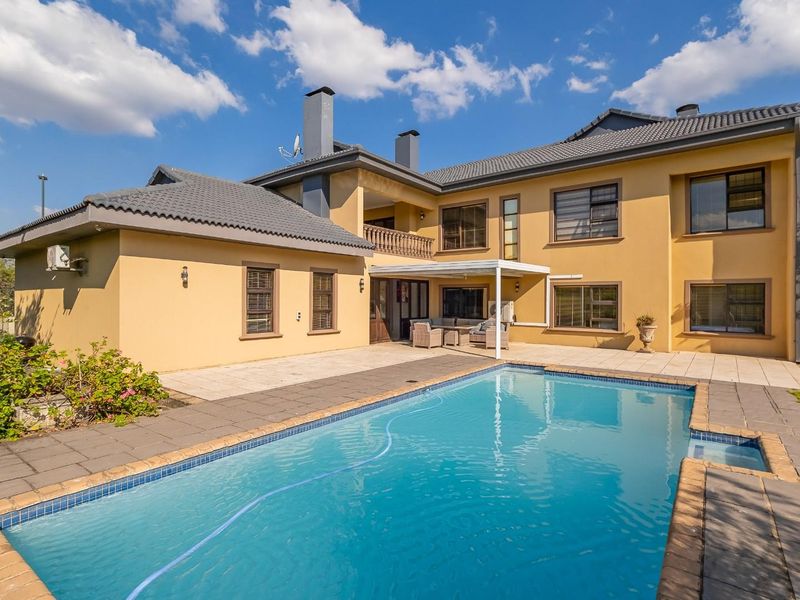 Rear view of the property featuring a swimming pool, paved patio area, balcony, and well-maintained exterior facade with a tiled roof.