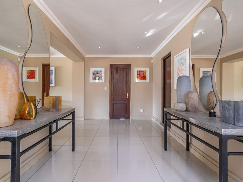 A bright and well-maintained entrance hall featuring polished tiled flooring, recessed downlighting, and a solid wood door.